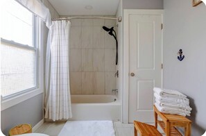 Un baño con bañera, cortina de ducha, una pila de toallas y un banco de madera.