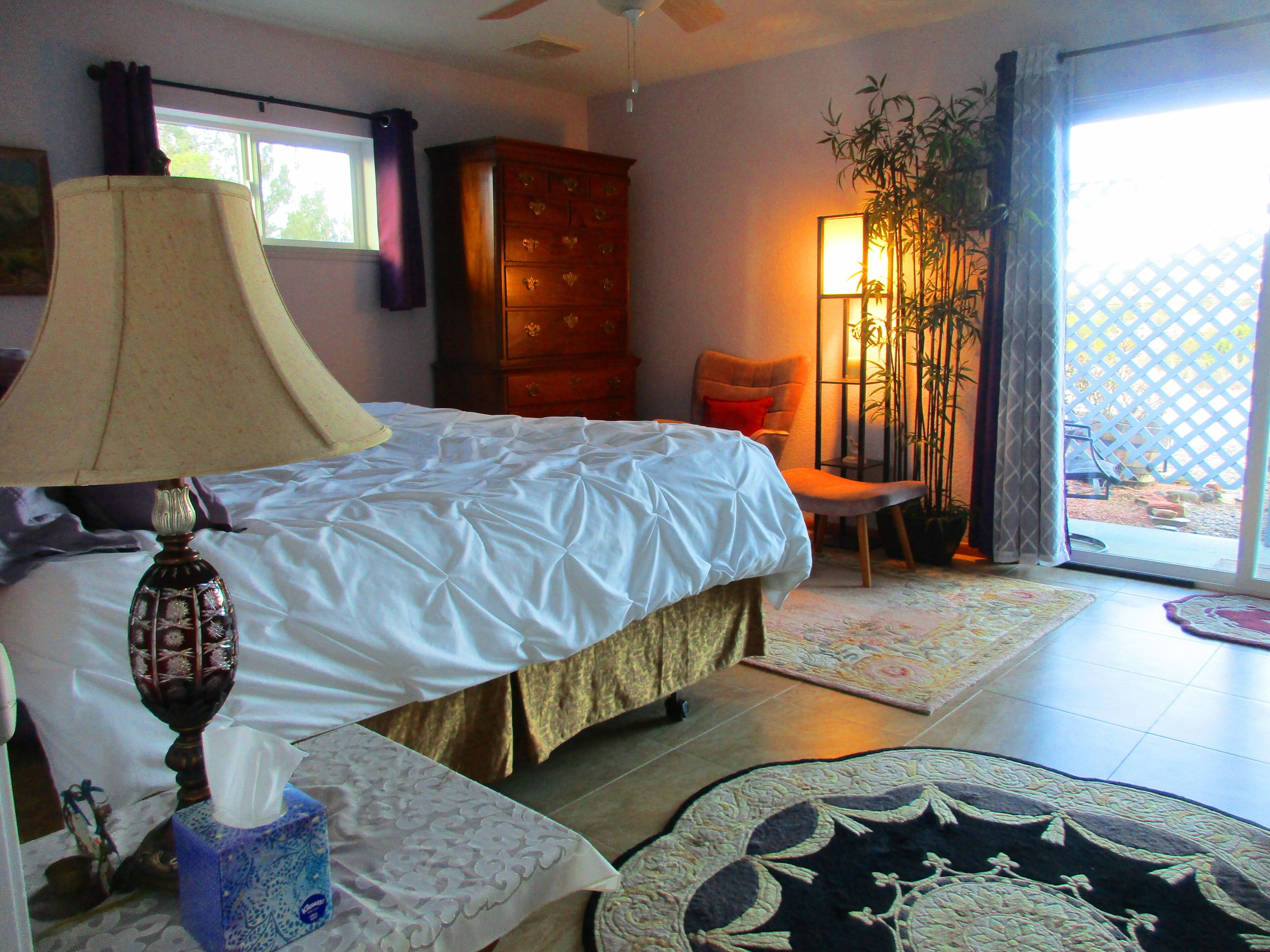 A bedroom with a bed, a nightstand, a dresser, a chair, and a view of the outside.