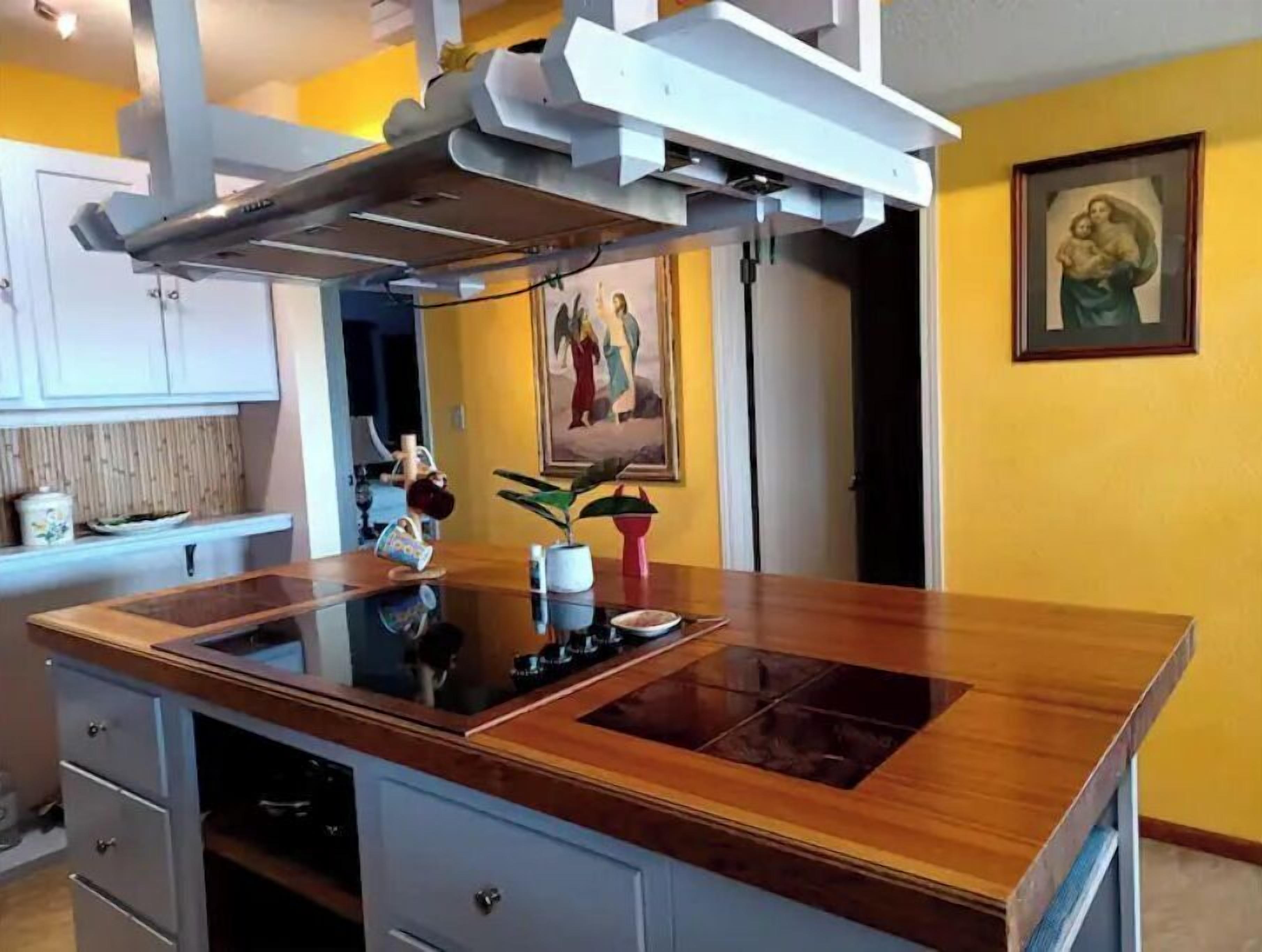 Uma cozinha com ilha central, armários brancos e uma parede amarela.