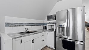 Una cocina compacta con muebles blancos, un refrigerador de acero inoxidable, un microondas y un horno empotrado.