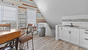 Una cocina moderna con armarios blancos, una mesa de comedor de madera y una escalera que sube a un nivel superior.
