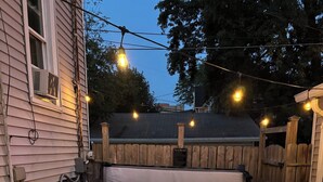 Un jacuzzi con un banco de madera al frente, rodeado por una valla de madera y luces de cadena.