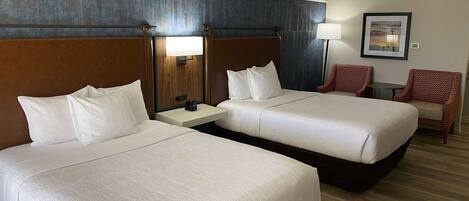Una habitación de hotel con dos camas, una mesita de noche, una lámpara y una silla.