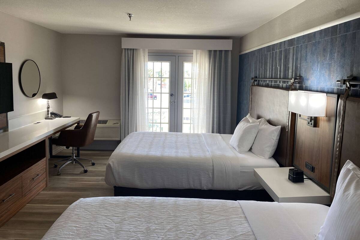 Een hotelkamer met twee bedden, een bureau, een stoel, een televisie en een raam met gordijnen.