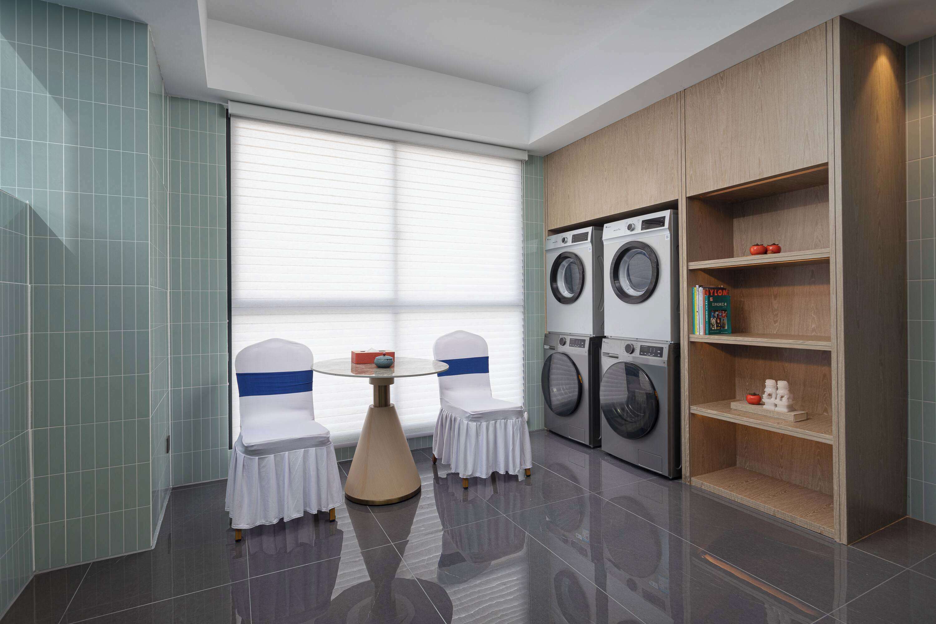 A modern laundry room with two chairs, a table, and a shelf with books and toiletries.