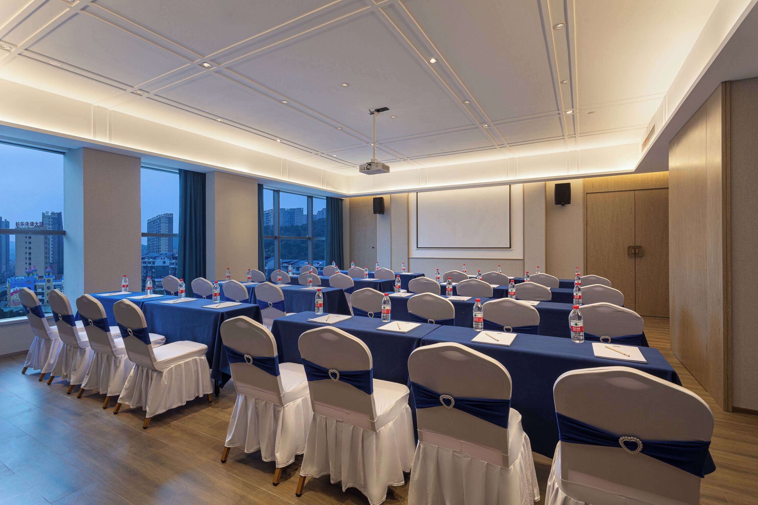 A conference room with multiple tables and chairs, large windows, and a city view.