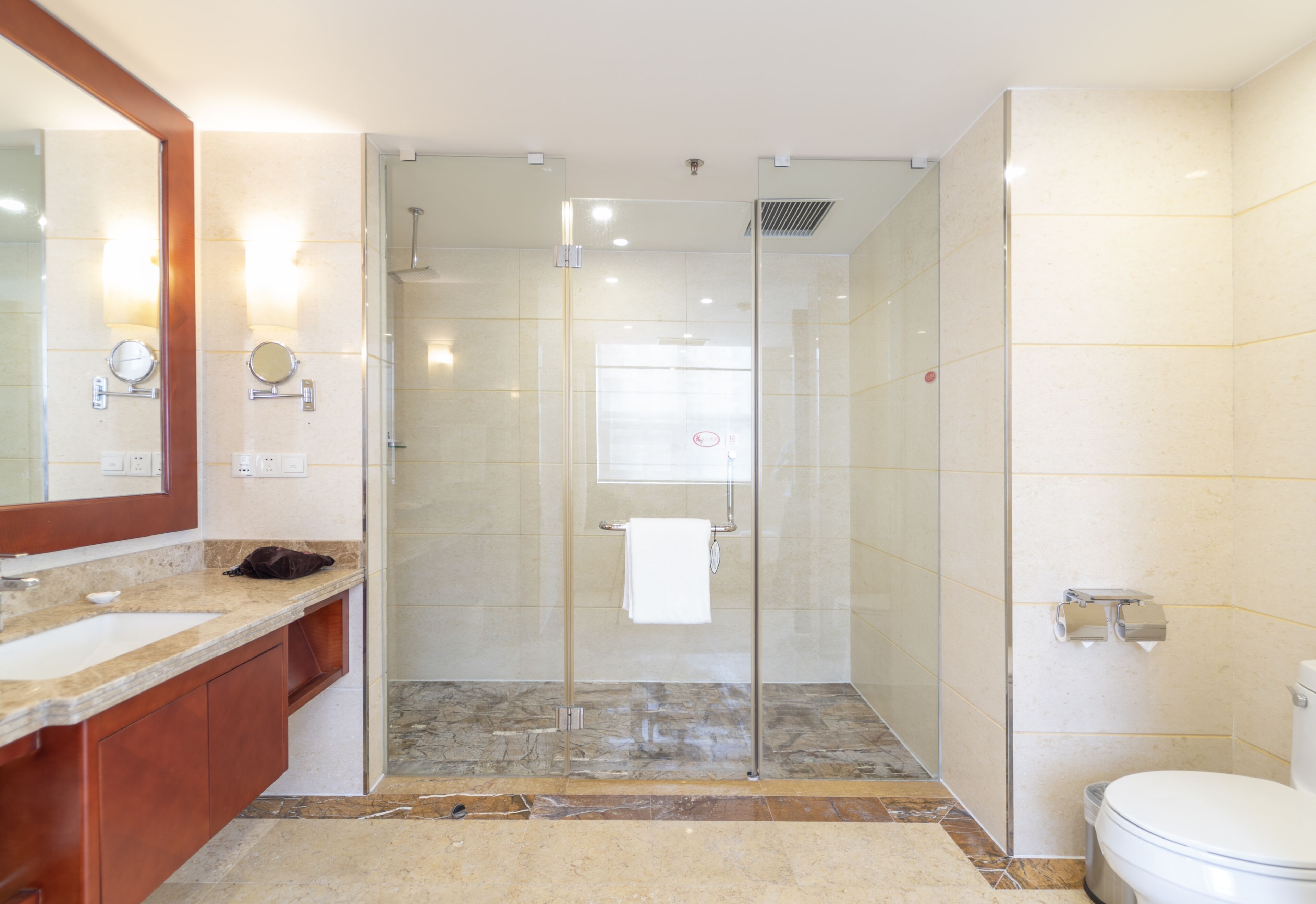 A modern bathroom with a glass-enclosed shower, a large mirror, and a white toilet.
