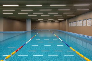An indoor swimming pool with lane dividers, overhead lighting, and informational posters on the walls.