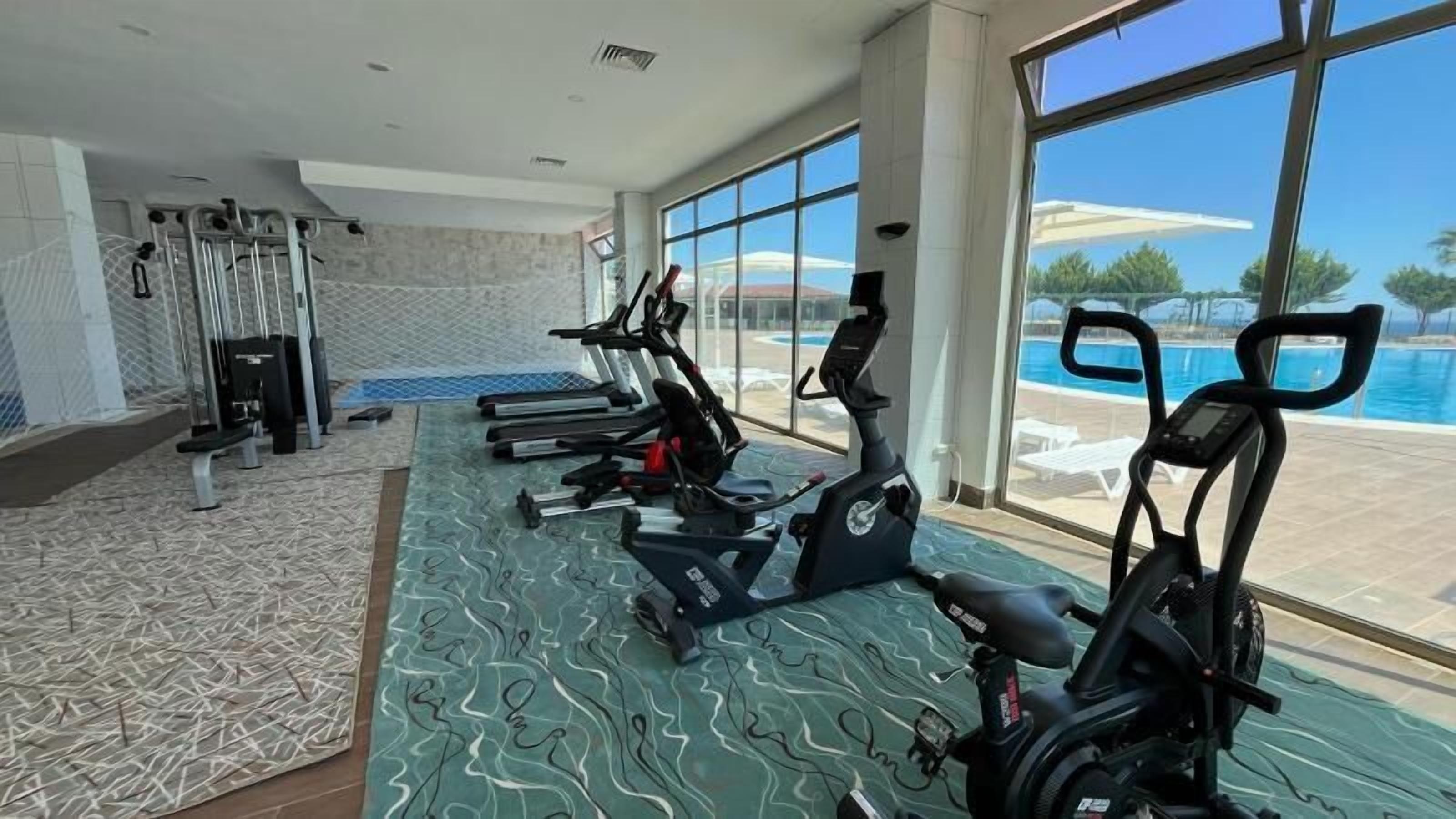 A gym with exercise equipment and a view of a pool.