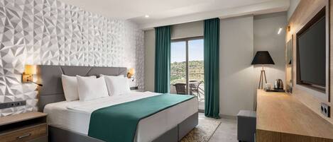 Una habitación de hotel moderna con una pared de diseño geométrico, una cama grande con una colcha verde, un escritorio con televisión de pantalla plana y un balcón con vistas al desierto.