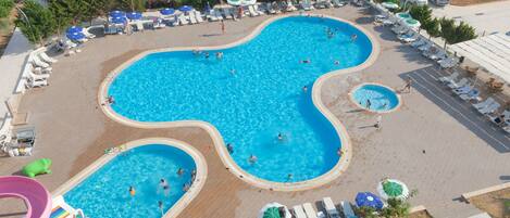 Una piscina grande y de forma irregular con múltiples carriles, rodeada de tumbonas y sombrillas.