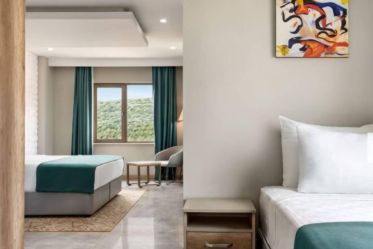 Una camera d'albergo con due letti, una scrivania, una sedia e un'ampia finestra con tende.