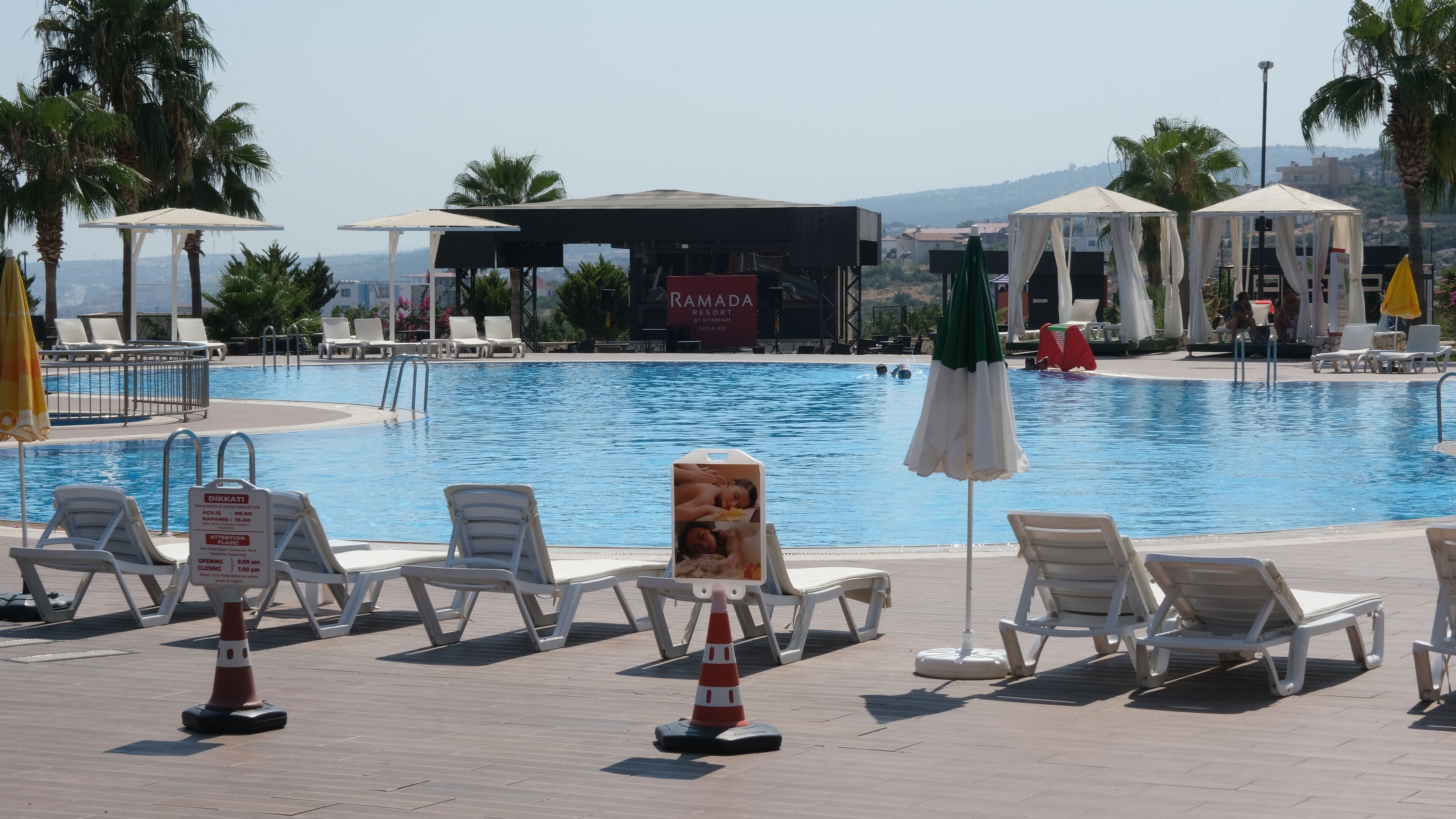 A pool area with lounge chairs, umbrellas, and a sign indicating the pool's opening and closing times.