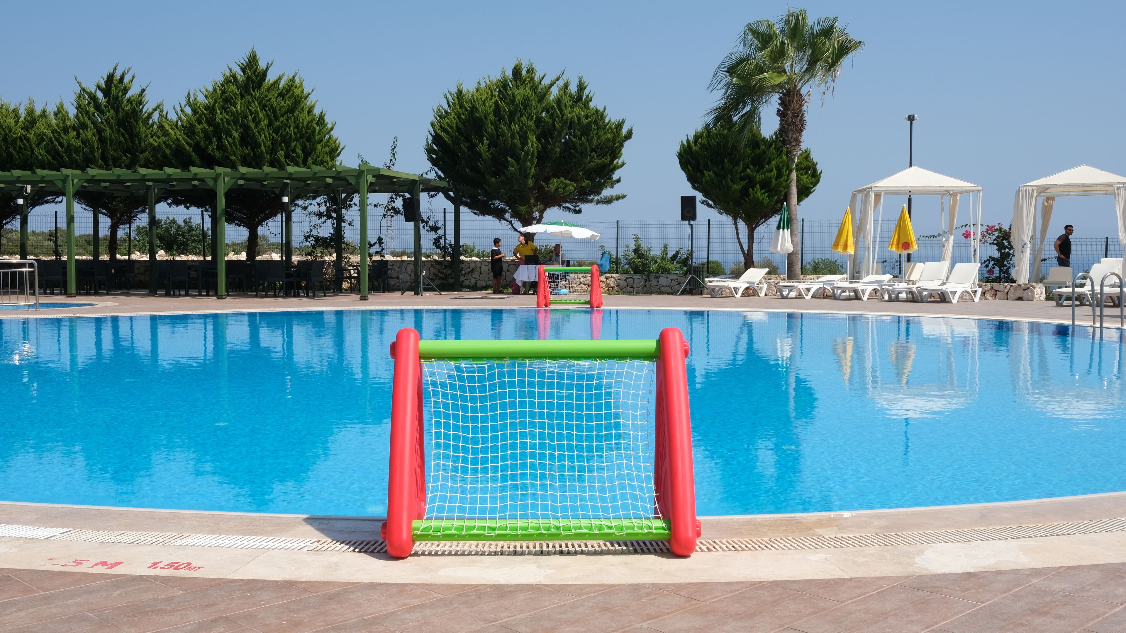 A swimming pool with a goalpost, lounge chairs, and a covered seating area.