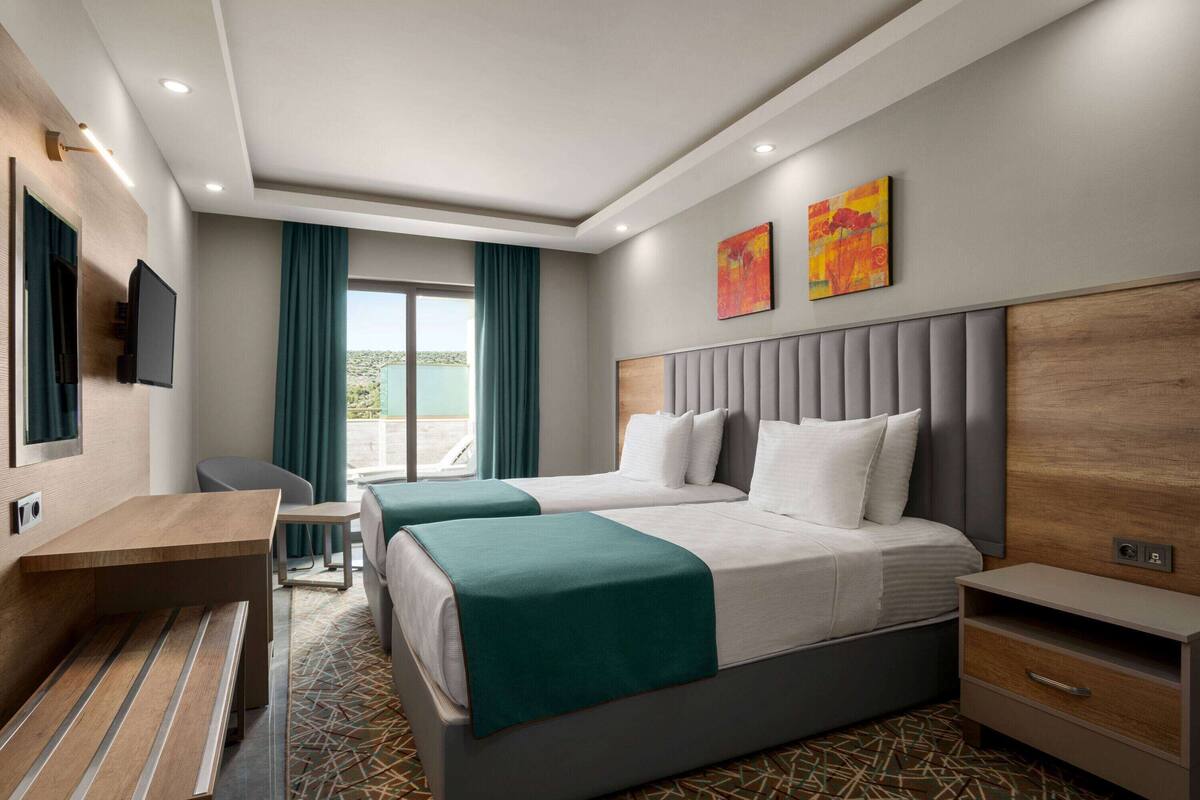 Ein Hotelzimmer mit zwei Betten, einem Schreibtisch, einem Fernseher und Bildern an den Wänden.