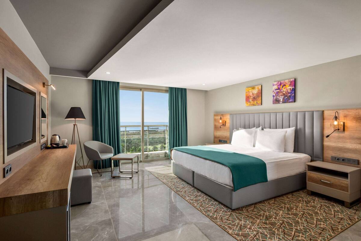 Ein modernes Hotelzimmer mit einem großen Bett, einem Schreibtisch, einem Sessel und Blick ins Freie.