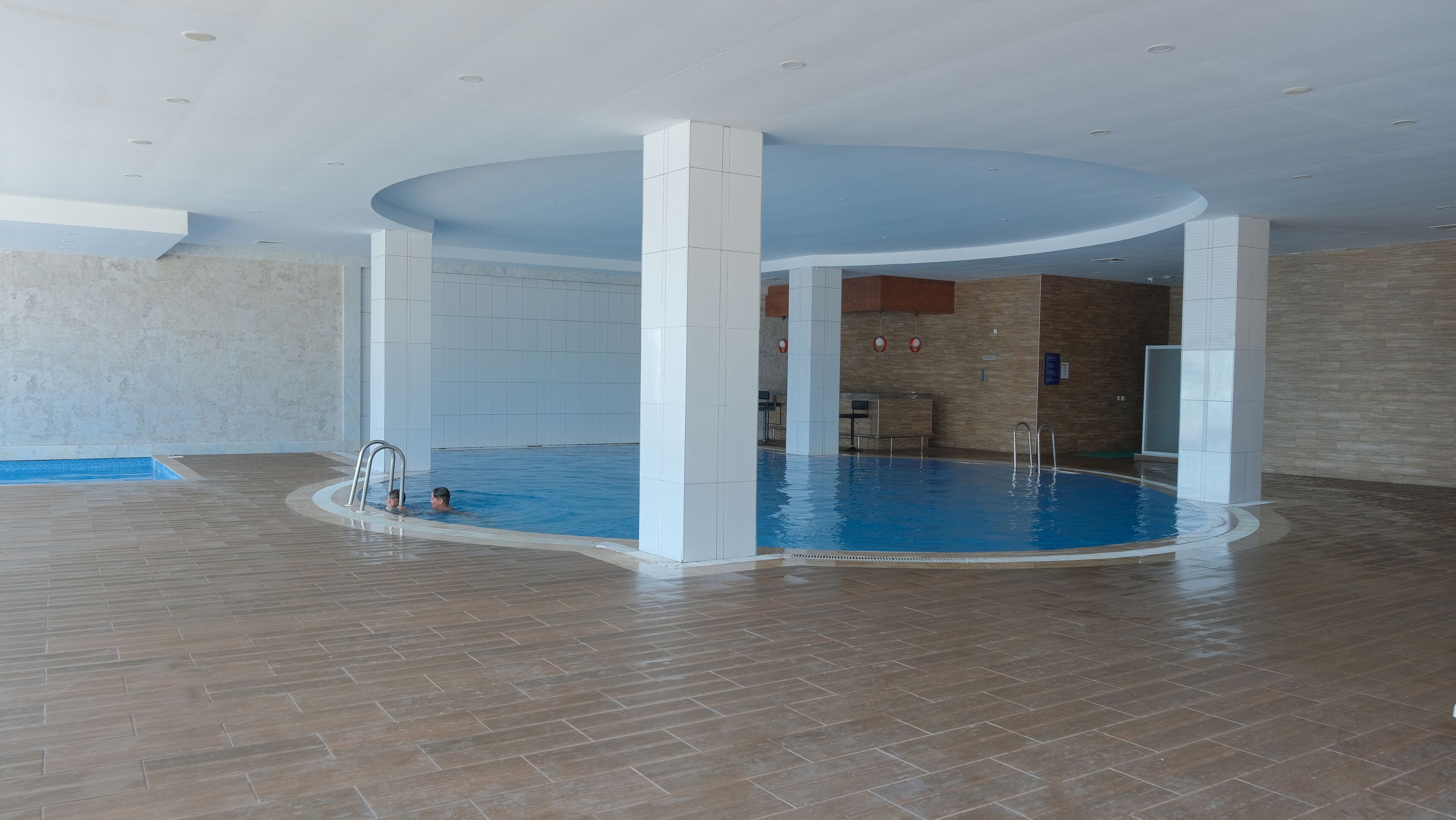 Una piscina interior con suelo de baldosas y una escalera de acceso.