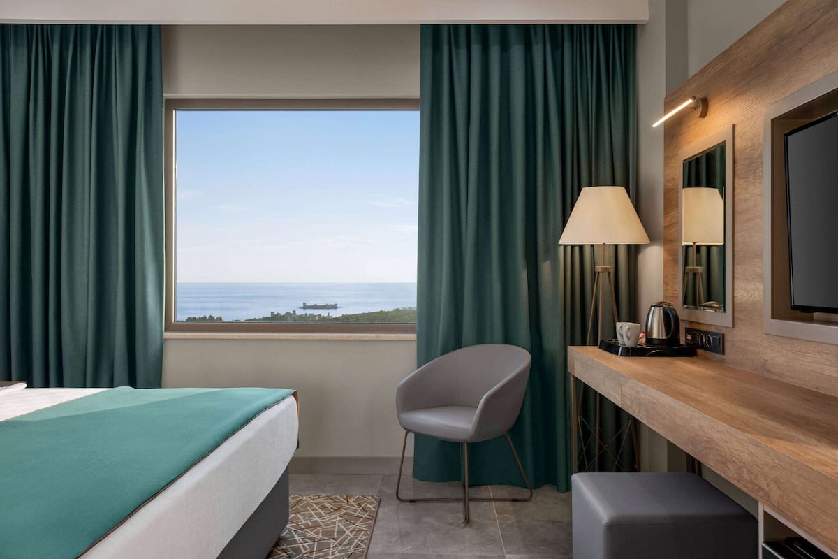 Ein Hotelzimmer mit Bett, Sessel, Schreibtisch mit Lampe, Fernseher und Meerblick.