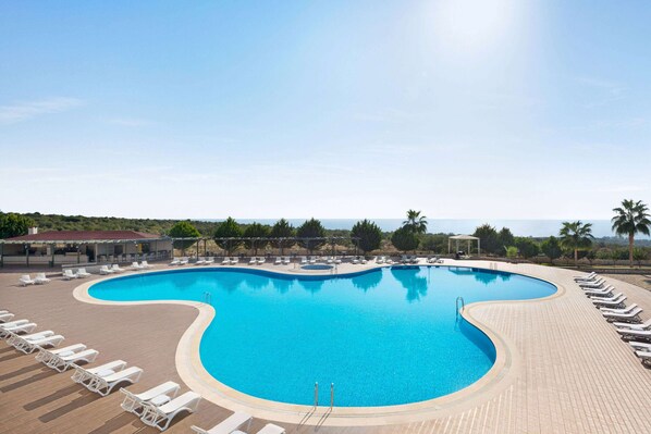 Una piscina grande y curvada con sillas de descanso y un área de estar techada.
