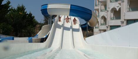 A water slide at a resort with a clear sky and a building in the background.
