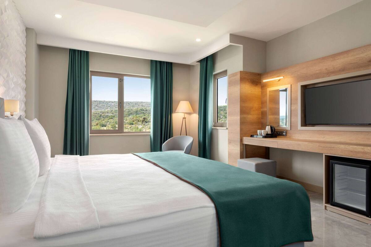 Ein modernes Hotelzimmer mit einem großen Bett, einem Schreibtisch, einem Stuhl, einem Fernseher und Blick auf die Stadt.