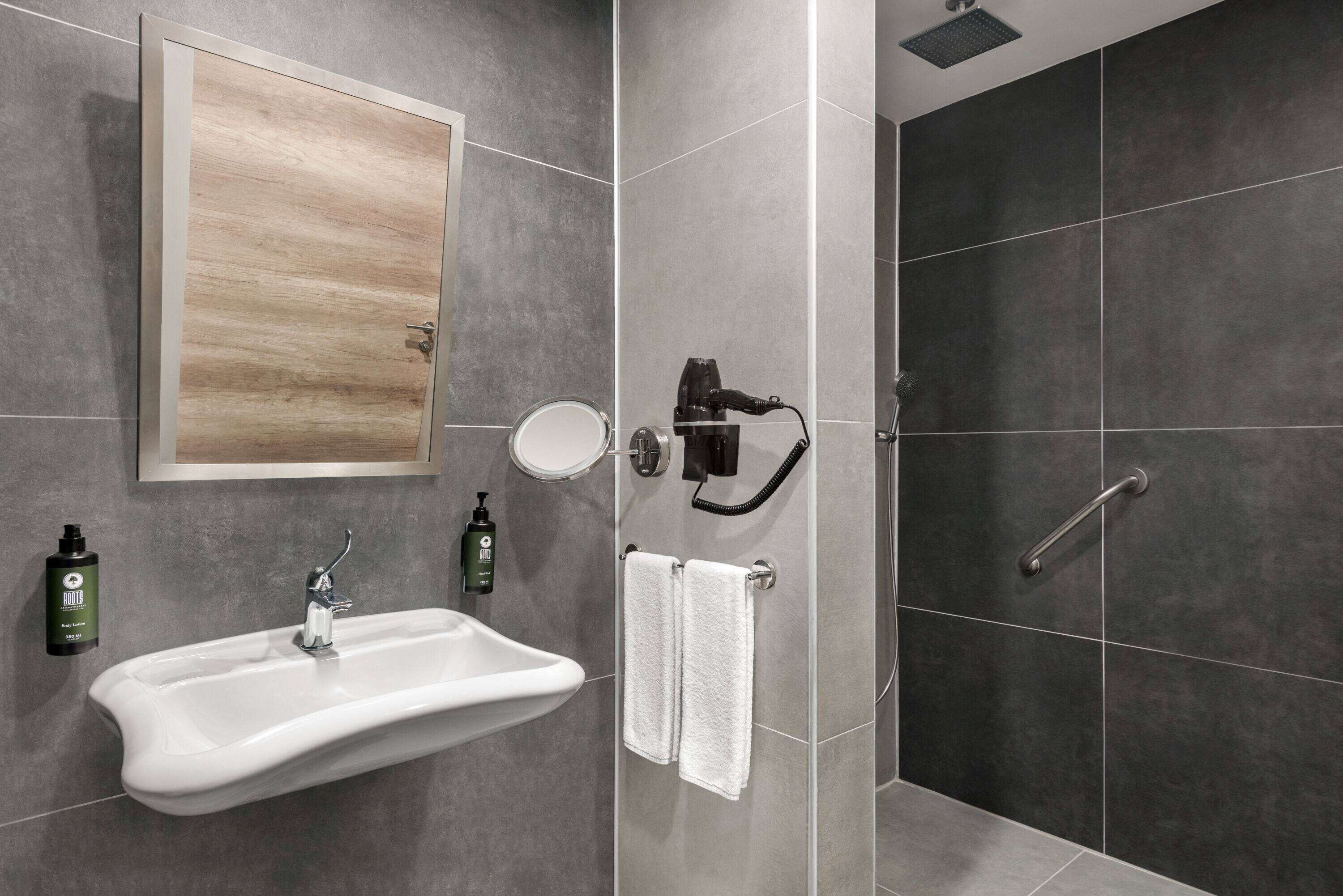 A modern bathroom with a white sink, a mirror, and a shower area.
