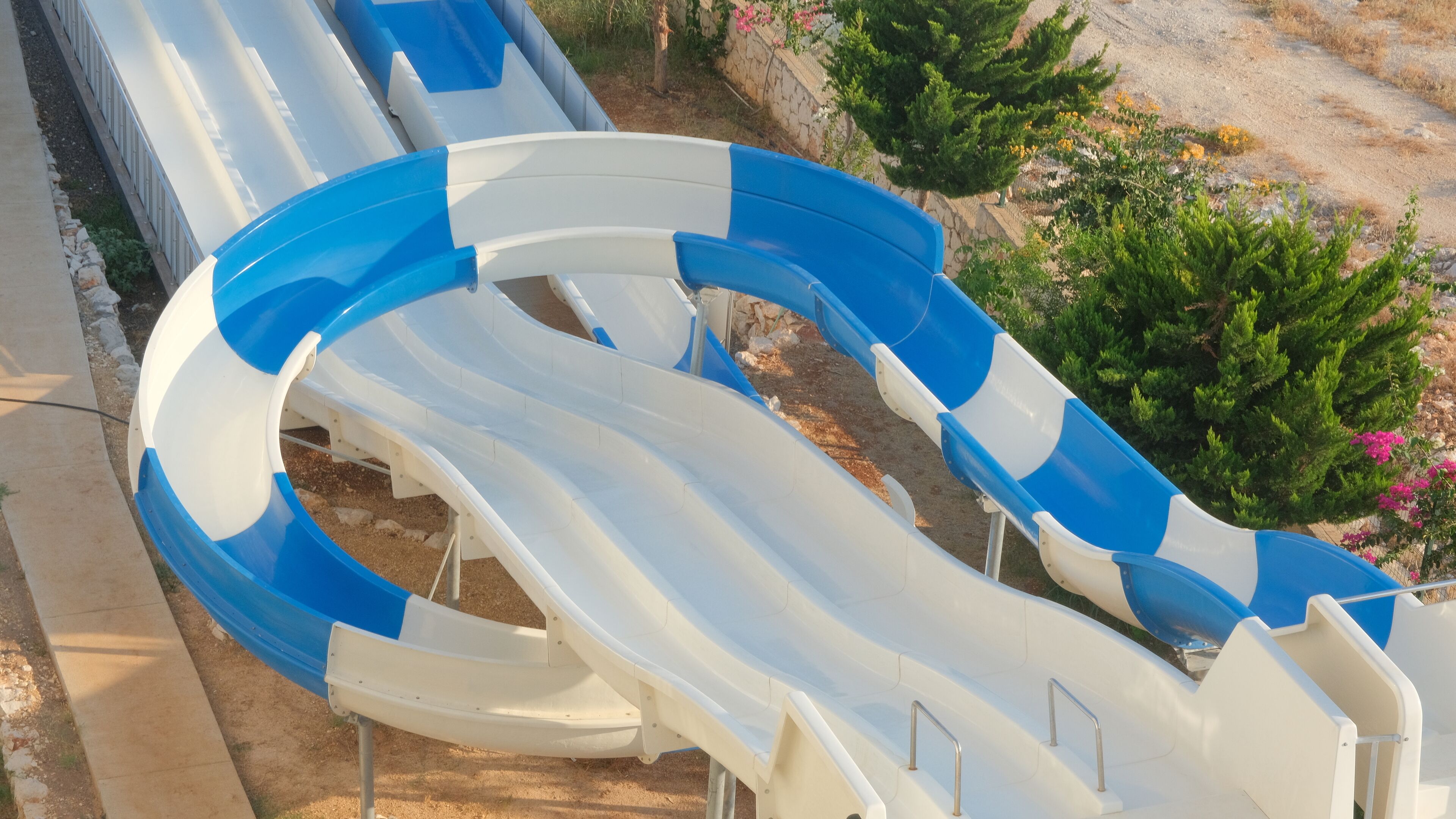 A series of blue and white water slides in a dry, rocky area with sparse vegetation.