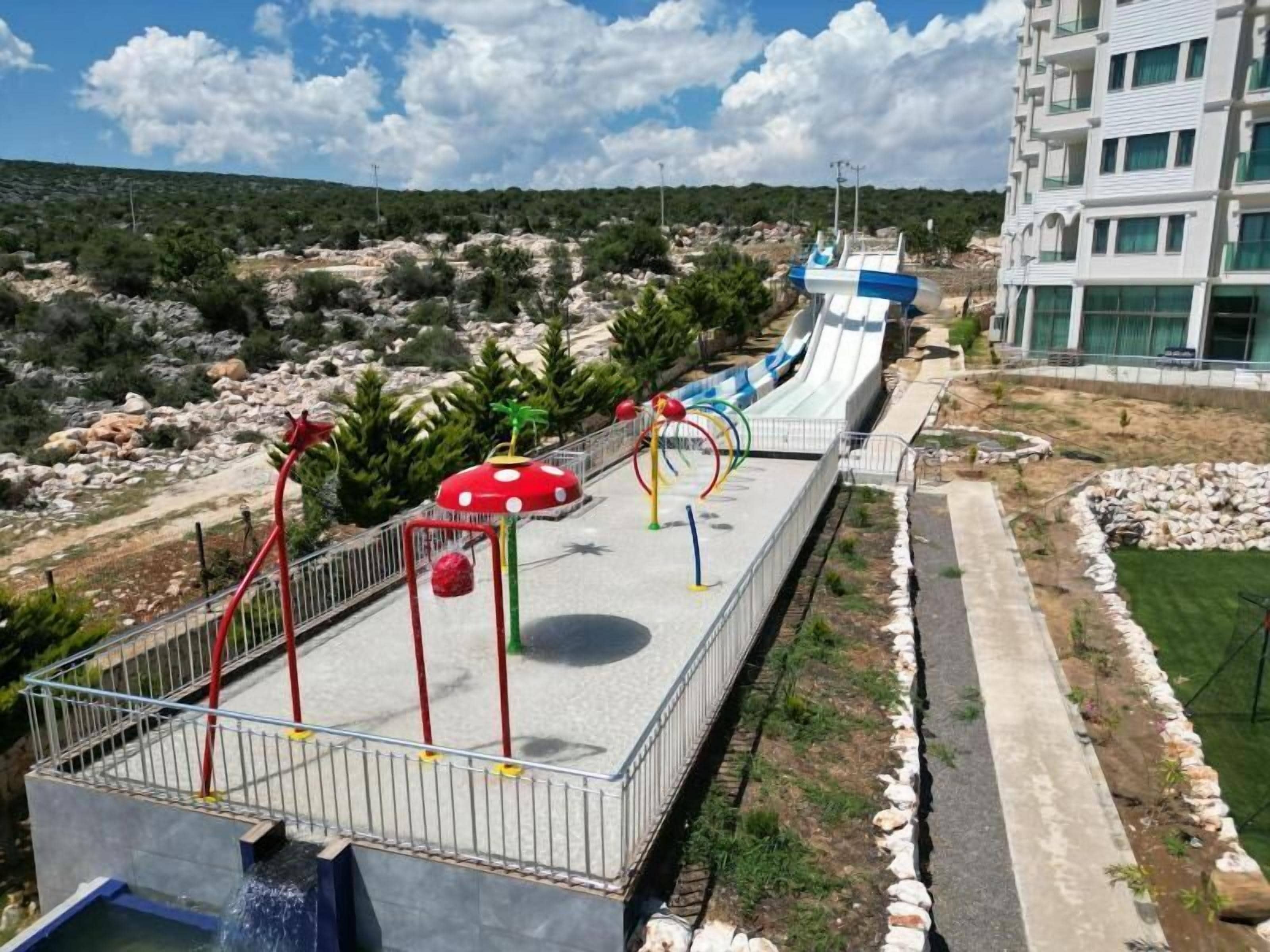 A water park with slides and play structures, surrounded by a landscaped area with rocks and greenery.