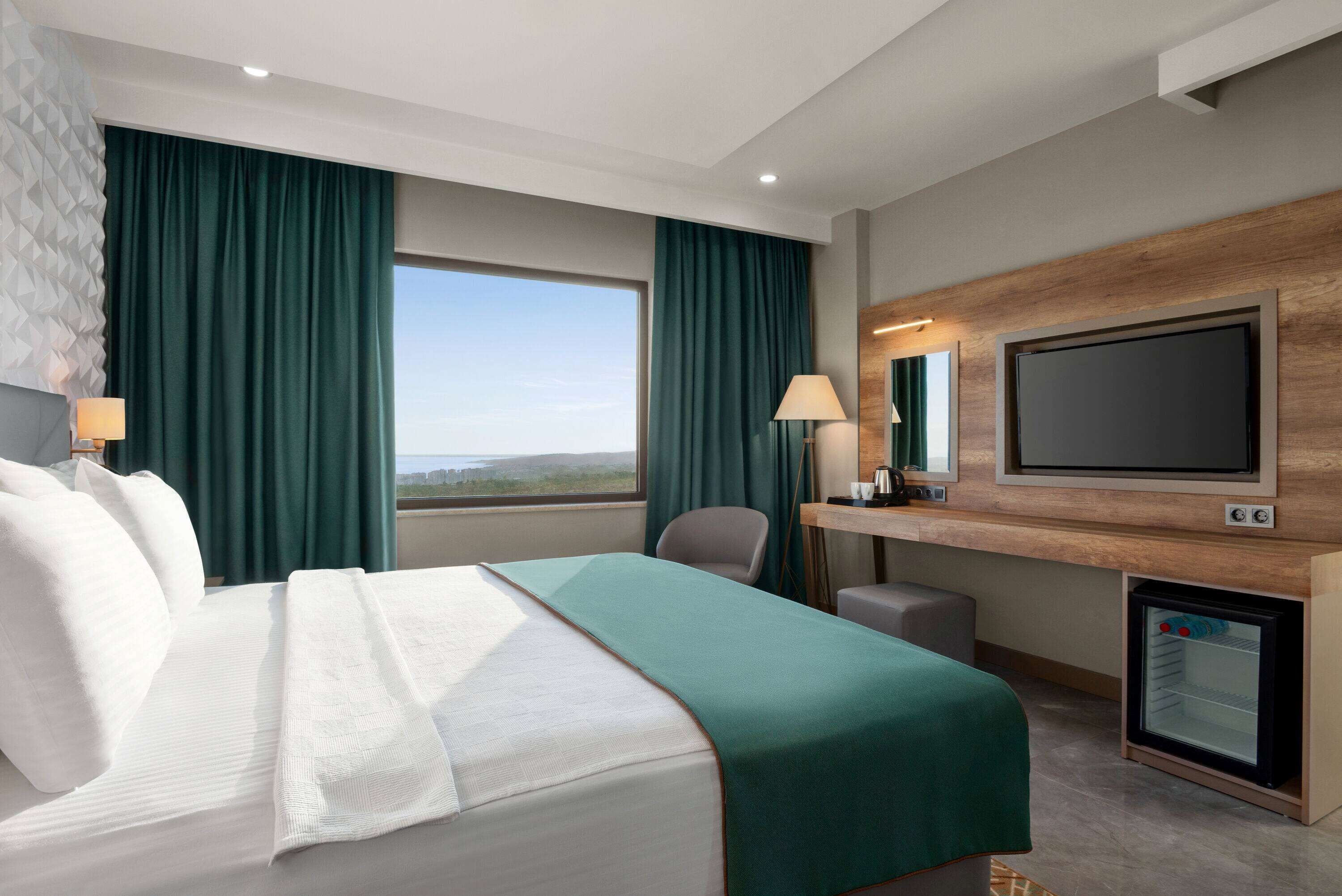 A hotel room with a bed, a desk, a TV, and a minibar.