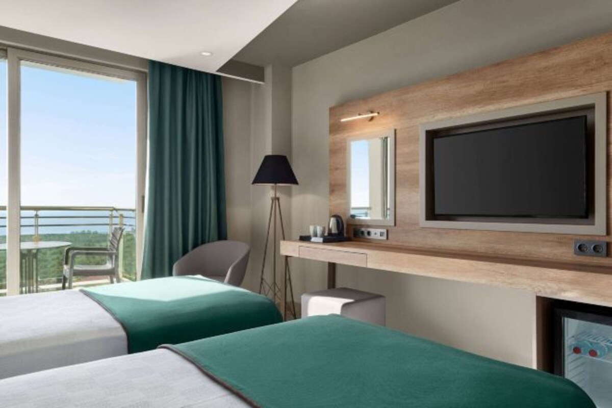 Une chambre d’hôtel avec deux lits, un bureau doté d’un téléviseur à écran plat, une lampe et une grande fenêtre donnant sur un paysage.