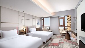 Habitación de hotel con dos camas, un escritorio, una silla, un televisor y un amplio ventanal con vistas a la ciudad.
