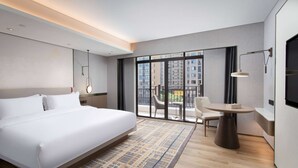 Habitación de hotel moderna con una cama grande, una mesa redonda y un balcón con vistas a la ciudad.
