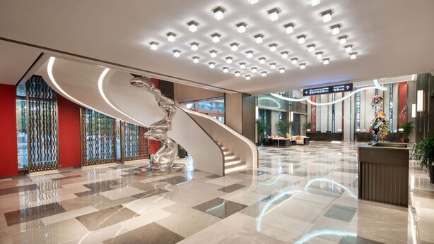 Un moderno vestíbulo de hotel con una escalera curva, una escultura metálica decorativa y un acceso despejado al ascensor.