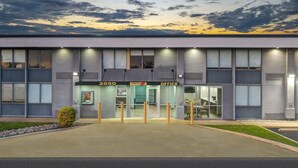 Un edificio de oficinas moderno con entrada de vidrio, un letrero que dice "2050 Office" y un césped bien cuidado.