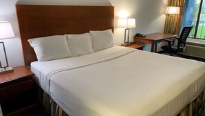 Een hotelkamer met een groot bed, twee nachtkastjes met lampen, een bureau met stoel, en een raam met gordijnen.