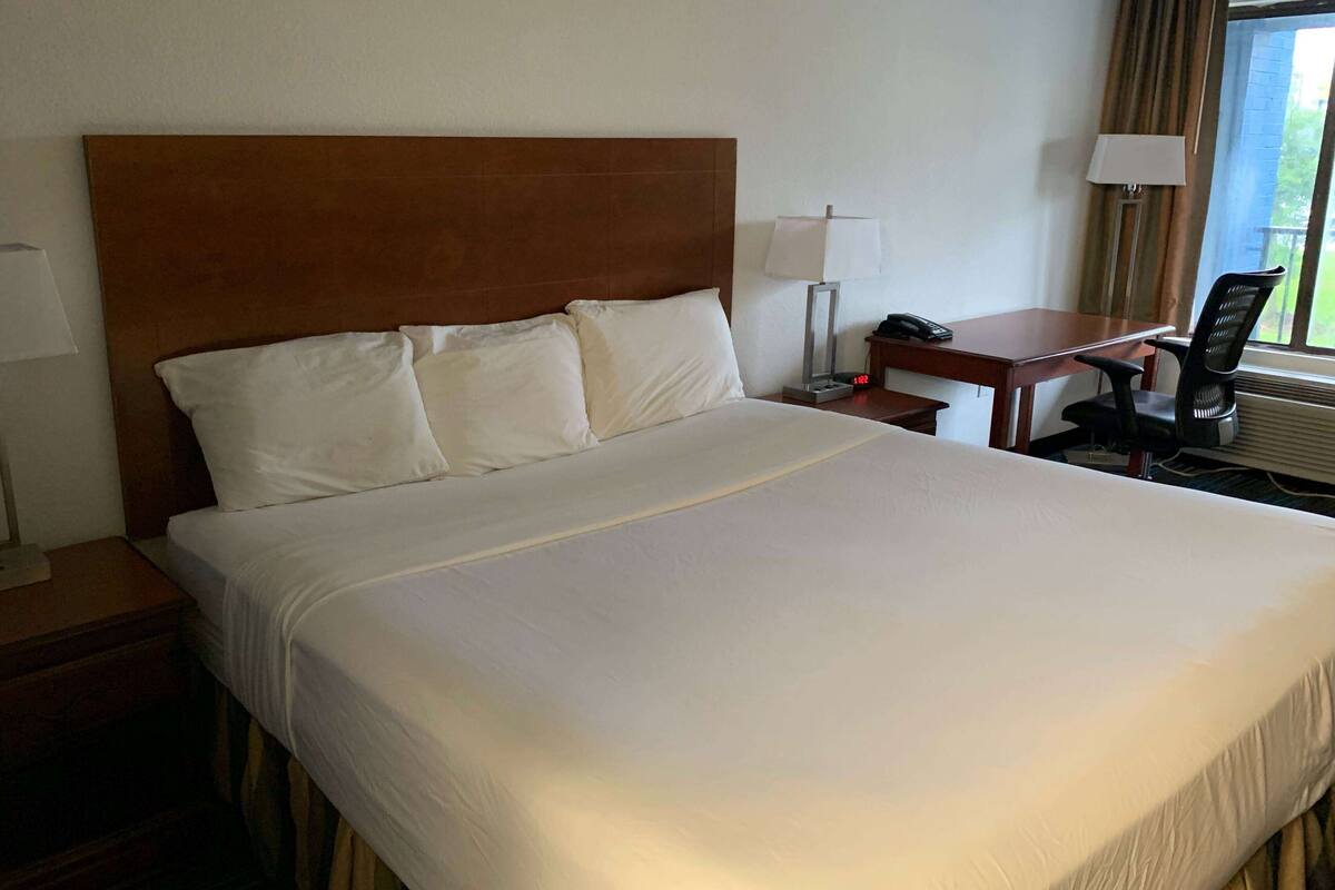 Ett hotellrum med en stor säng, ett skrivbord med en stol, en telefon och en lampa.