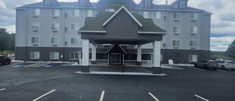 A multi-story hotel with a central entrance, parking lot, and several vehicles parked in the lot.