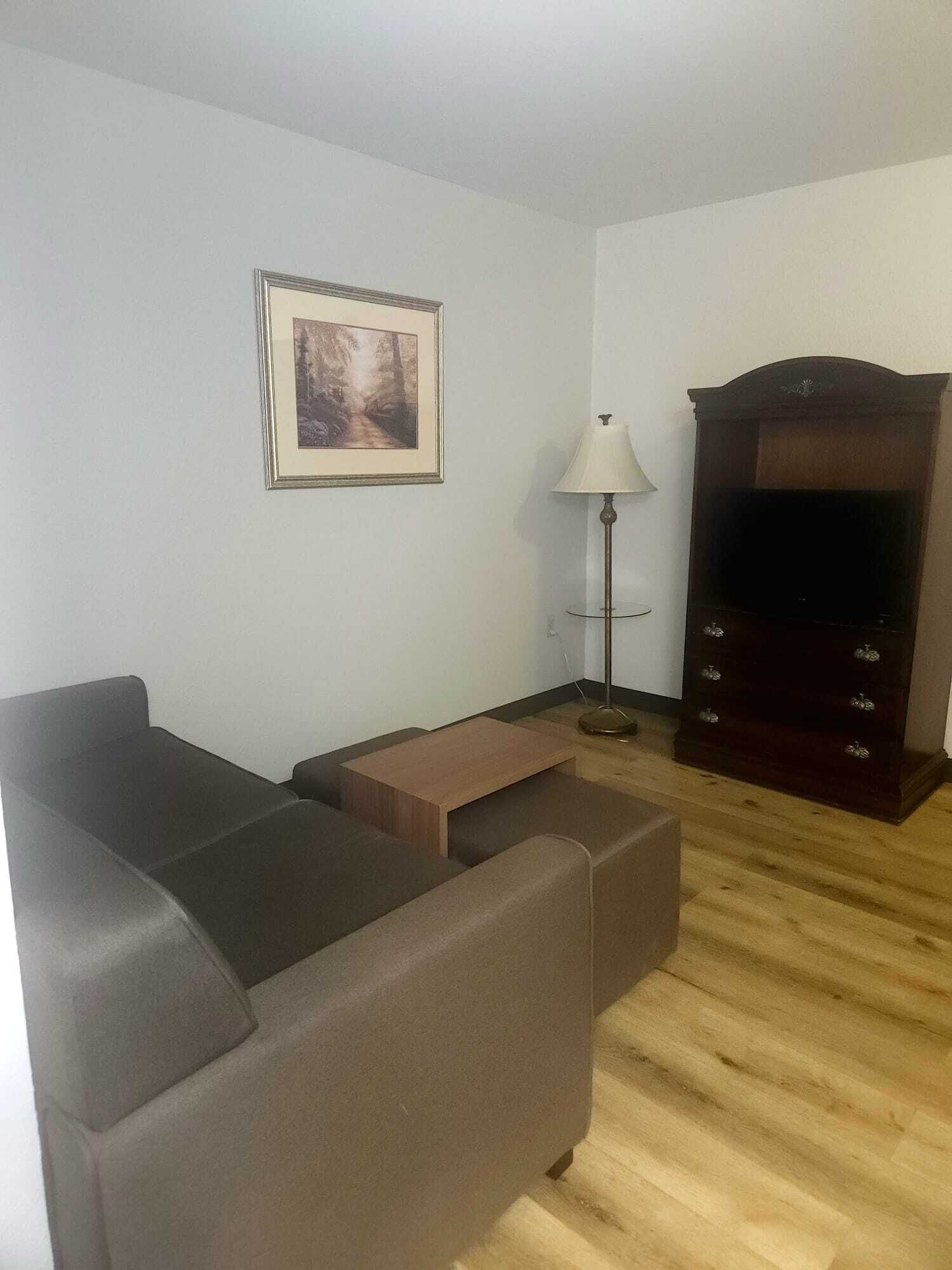 A living room with a sofa, a small table, a lamp, a TV stand, and a framed picture on the wall.