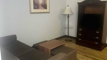 A living room with a sofa, a small table, a lamp, a TV stand, and a framed picture on the wall.