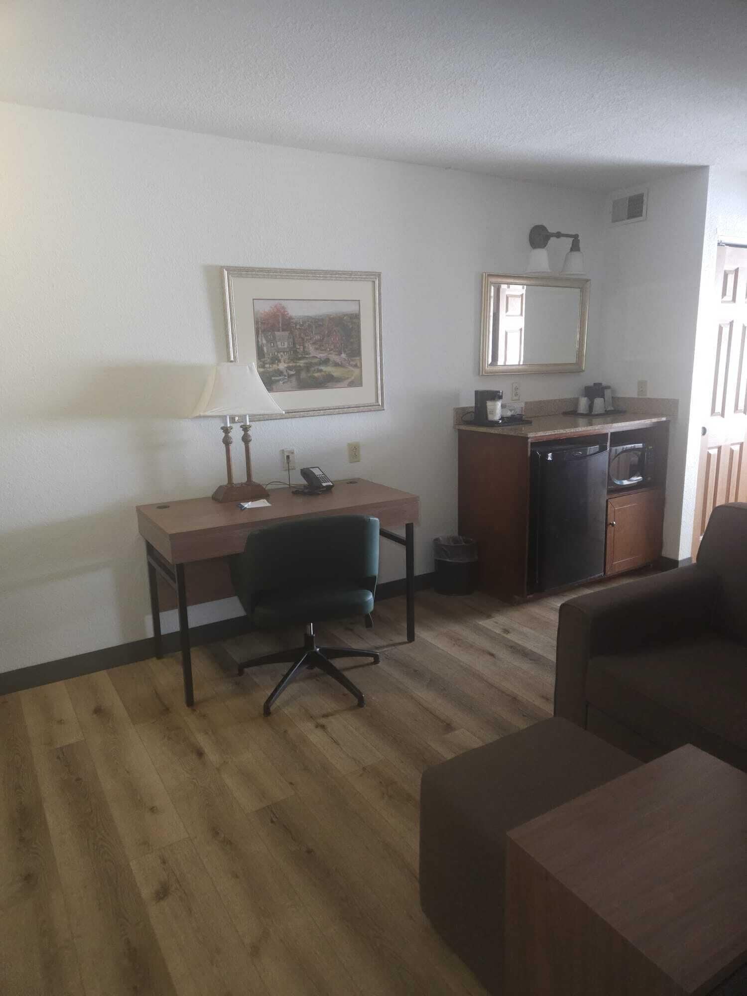 Une chambre d’hôtel compacte comprenant un bureau en bois, un fauteuil de bureau noir, une table à manger, un four à micro-ondes et une petite kitchenette.