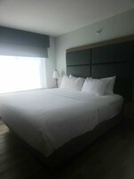 Una cama grande con cabecera oscura, ropa de cama blanca y una lámpara de noche.