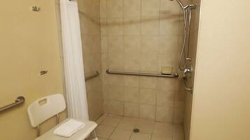 A wheelchair-accessible shower stall with a grab bar, a white chair, and a towel.