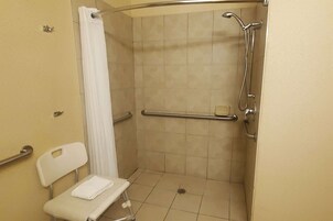 Cabina de ducha accesible para silla de ruedas con barra de apoyo, una silla blanca y una toalla.