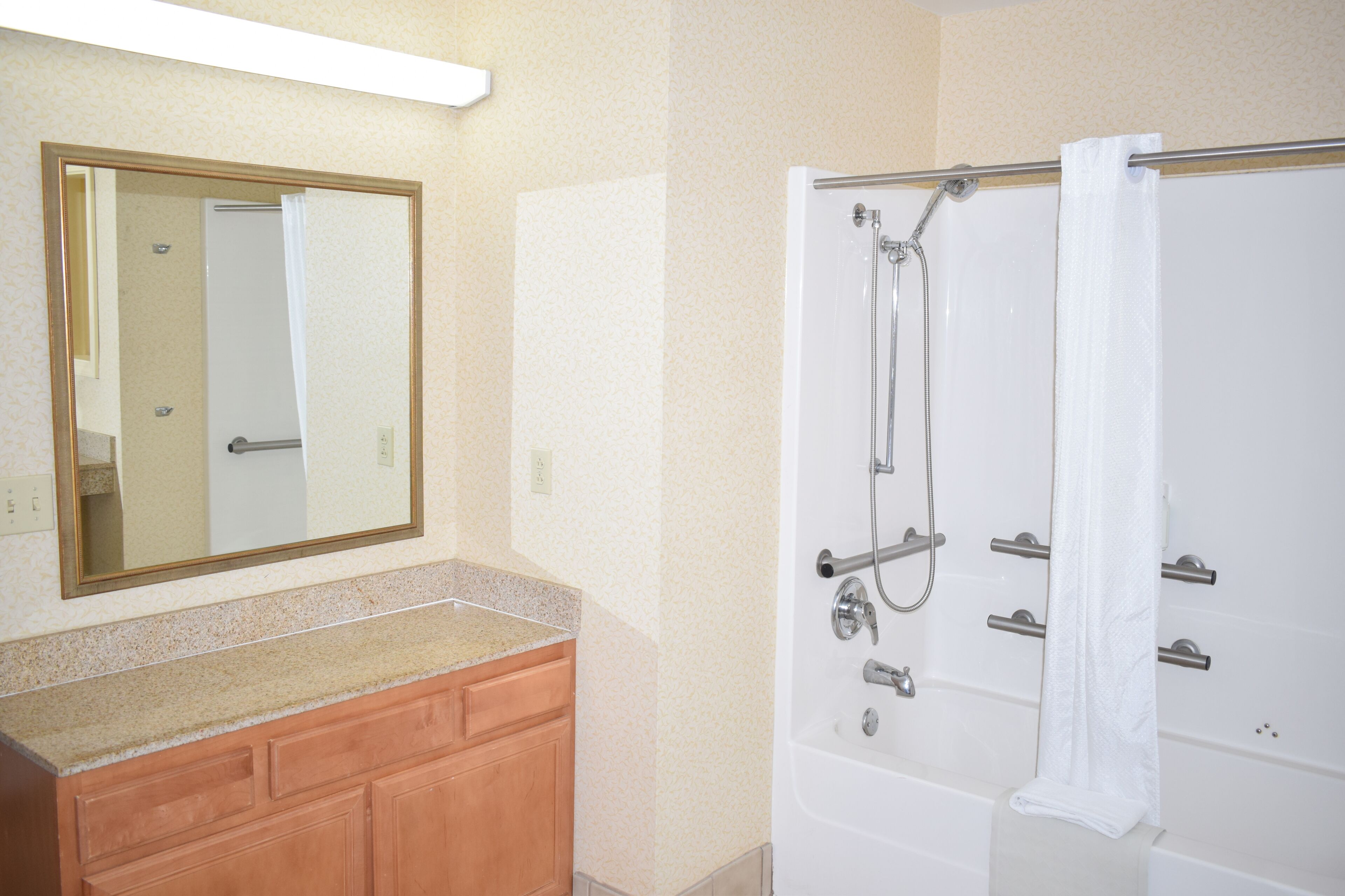 A bathroom with a wooden vanity, a large mirror, and a walk-in shower with a curtain.