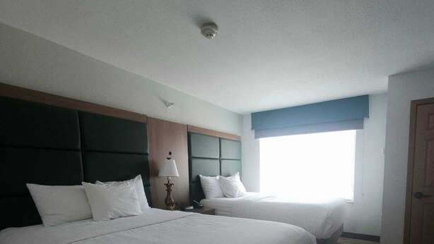 Habitación de hotel con dos camas, piso de madera, ventana con vistas y una puerta.