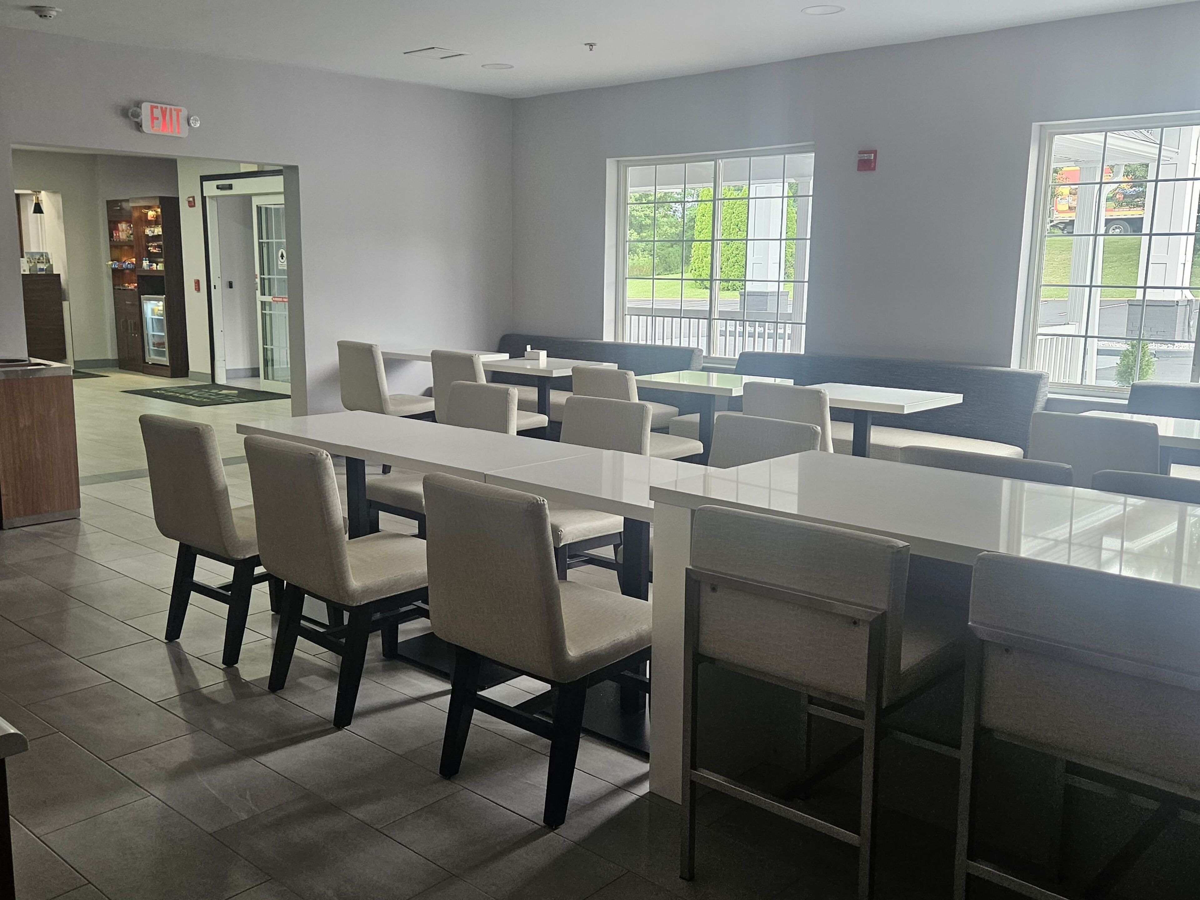 A spacious indoor area with multiple seating arrangements, including tables and chairs, and a visible exit sign.