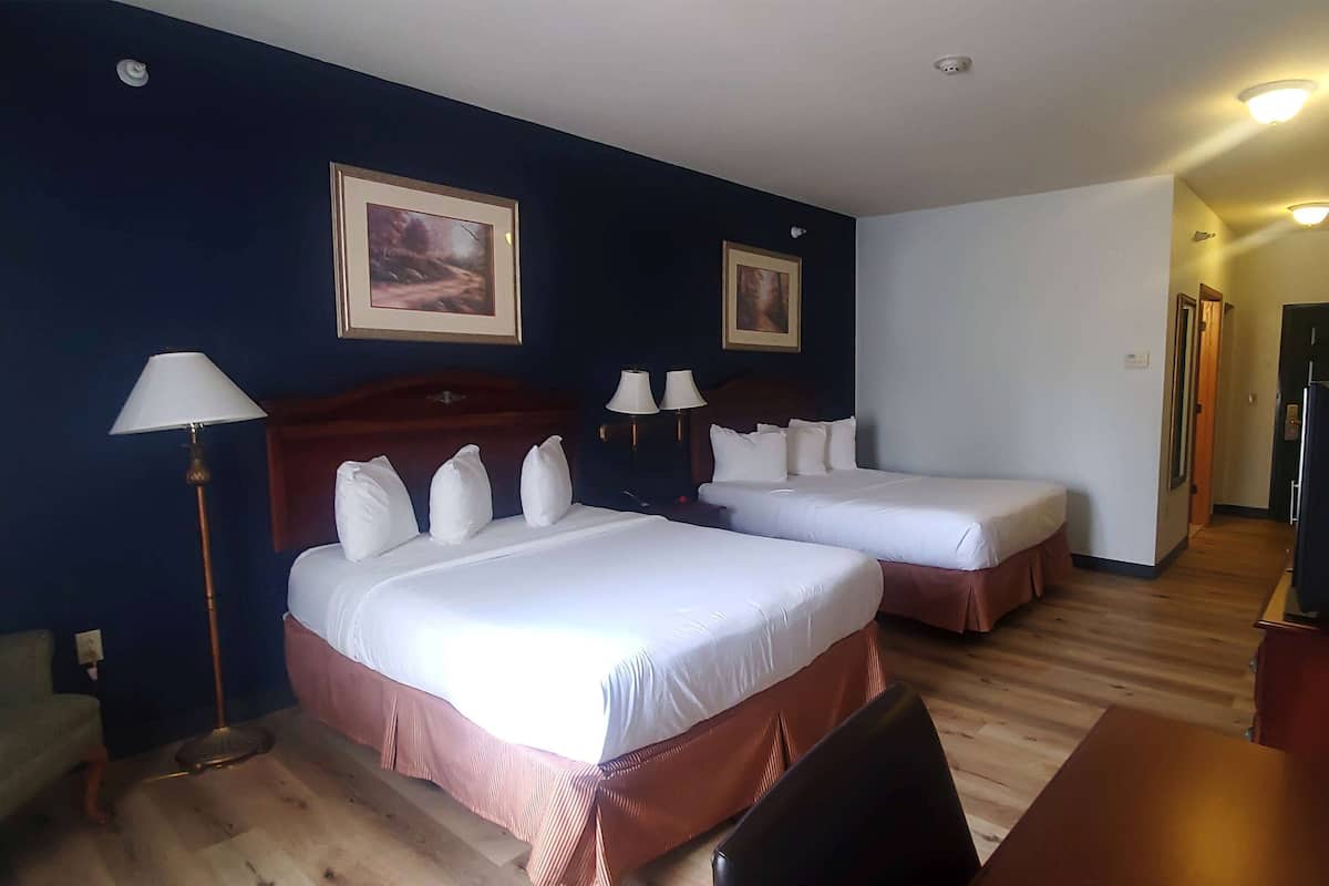 A hotel room with two beds, a desk, a chair, and two lamps.