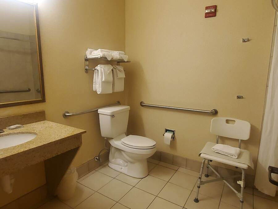 A bathroom with a sink, toilet, and a wheelchair-accessible chair.