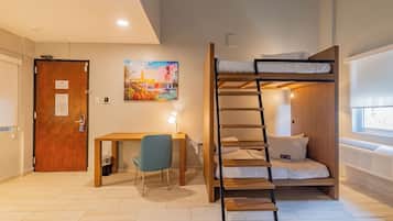 A room with a bunk bed, a desk with a chair, a painting on the wall, and a door with a notice.