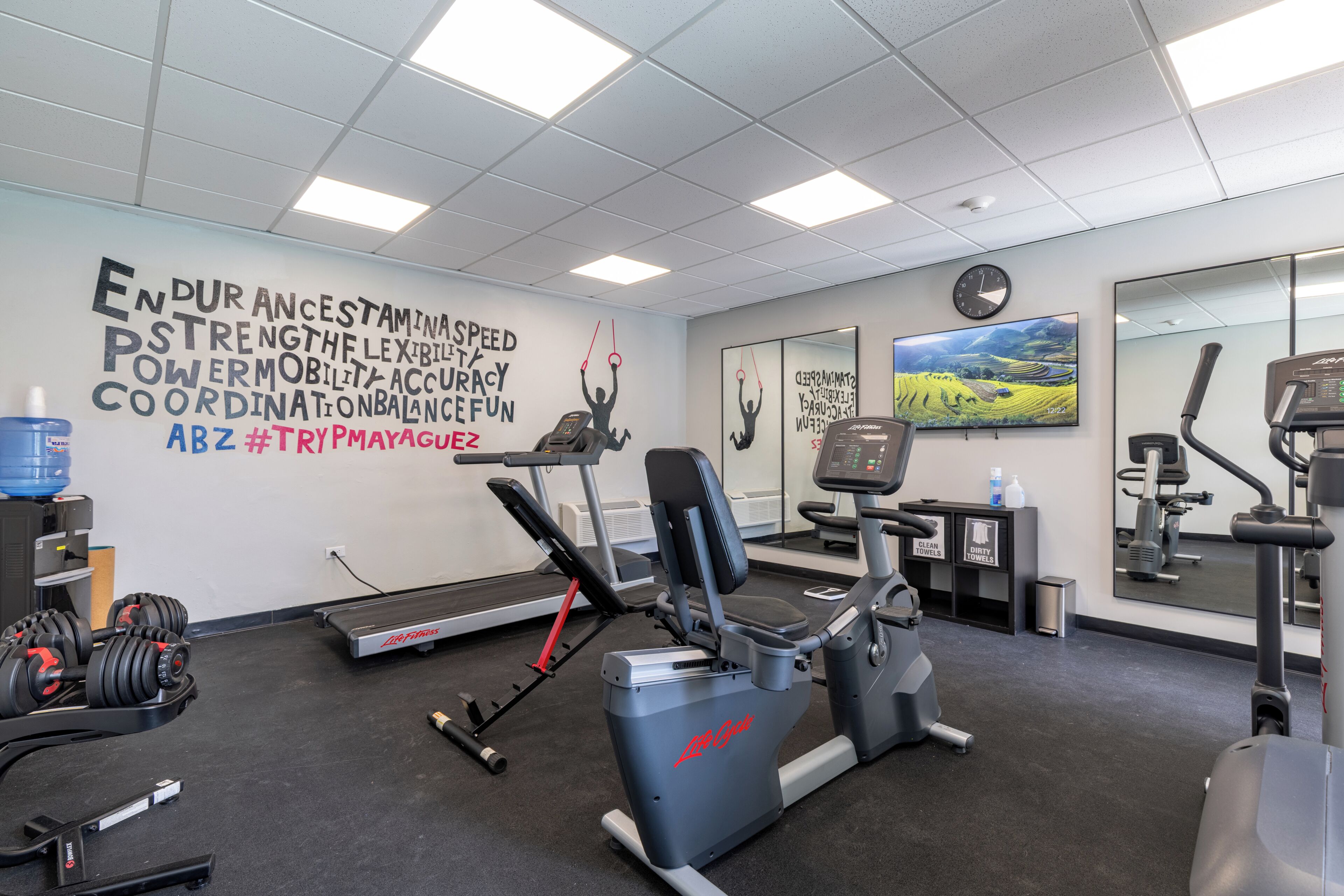 Ein Fitnessraum mit Trainingsgeräten, einem Wasserspender und motivierenden Wandbildern.
